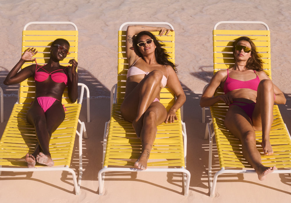 models wearing pink bathing suits laying on yellow beach chairs