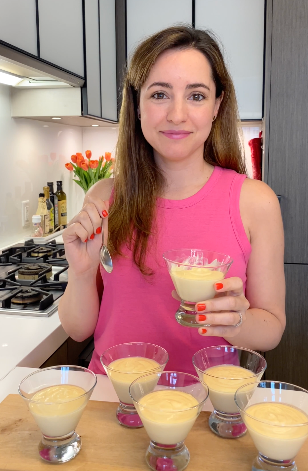 woman in a kitchen holding a cup of passionfruit mousse and a spoon