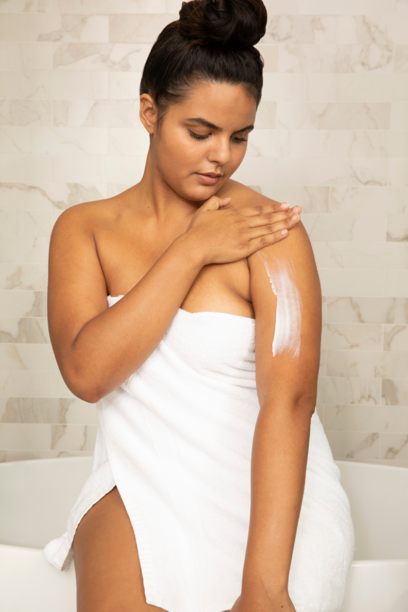 woman in bathroom wearing a towel and applying cream to her arm