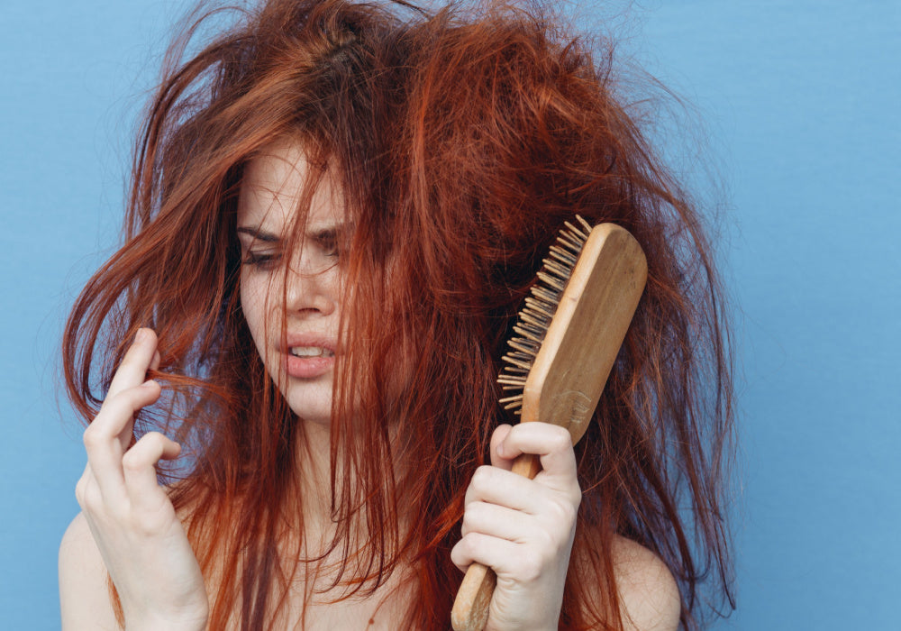 woman with messy and frizzy hair holding a brush looking disturbed by her hair.