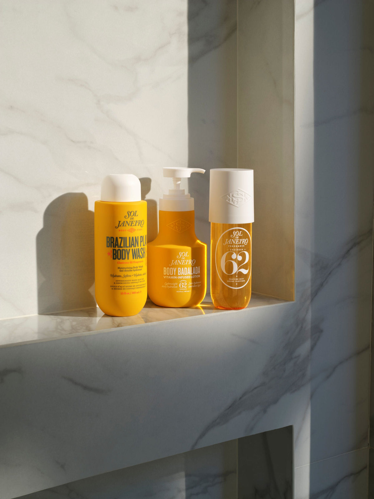 Three yellow sol de janeiro bottles with pump dispensers on a marble shelf