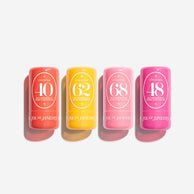 Four cylindrical cosmetic tubes in coral, yellow, pink, and magenta, arranged in a row on a light gray background. Each tube has a white oval label with numbers 40, 62, 68, and 48, and the brand name Sol de Janeiro is visible near the bottom.