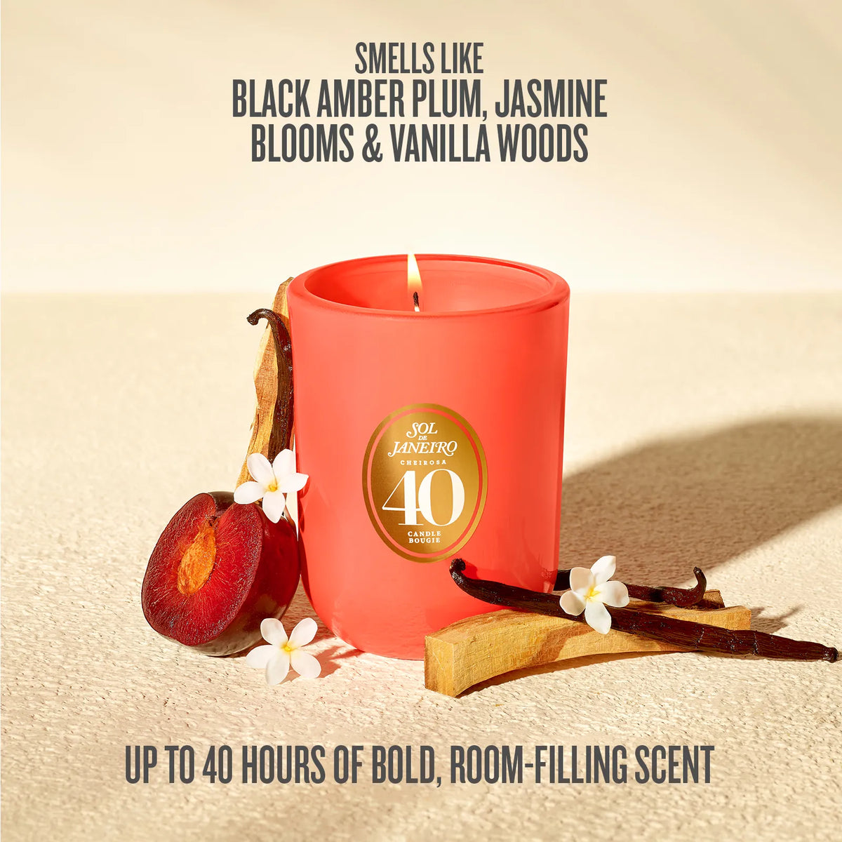 A red candle jar with a gold circular '40' medallion, styled with a sliced plum, vanilla pods, and small white flowers on a beige textured surface. Text above reads 'SMELLS LIKE BLACK AMBER PLUM, JASMINE BLOOMS & VANILLA WOODS' and text below reads 'UP TO 40 HOURS OF BOLD, ROOM-FILLING SCENT'.