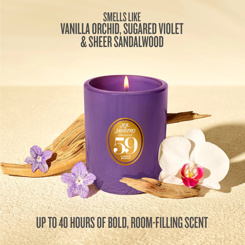 A purple jar candle with a lit flame and a gold circular label reading '59 SCENTS' is styled on a beige surface with dried wood pieces, purple flowers, and a white orchid. Text above says 'SMELLS LIKE VANILLA Orchid, SUGARED VIOLET & SHEER SANDALWOOD' and text below says 'UP TO 40 HOURS OF BOLD, ROOM-FILLING SCENT'.