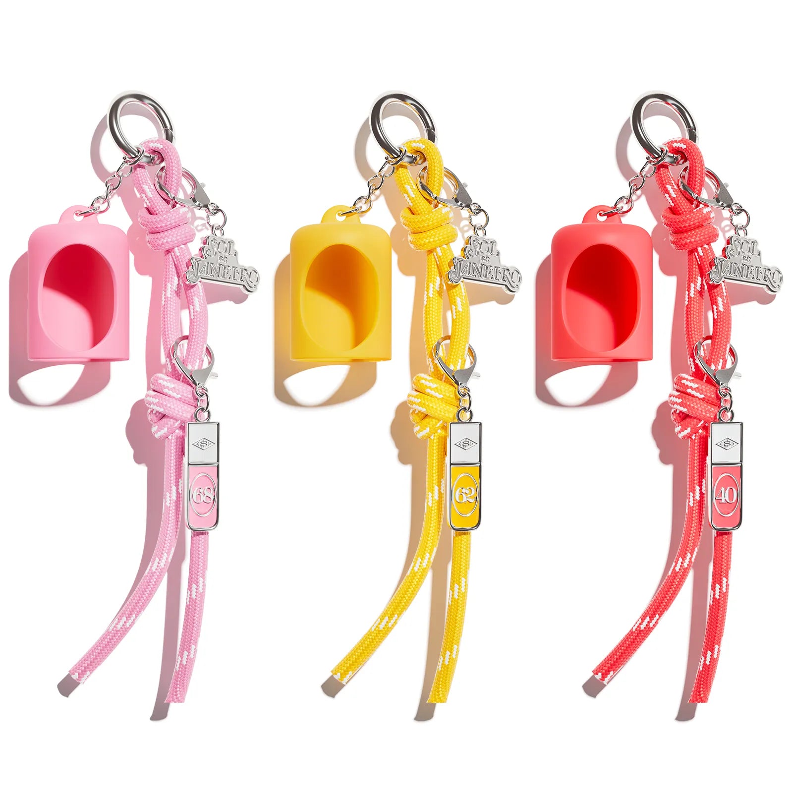 Three small silicone whistle keychains in pink, yellow, and red-orange, each with a braided strap and silver-tone keyring, shown on a white background.