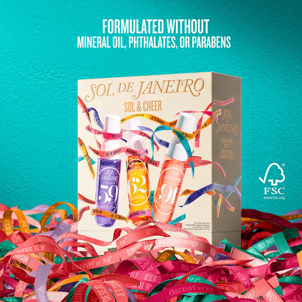 A boxed beauty product labeled SOL DE JANEIRO / SOL & CHEER stands upright on a bed of colorful ribbon strands against a bright turquoise background. The box shows three illustrated bottles in purple, orange, and peach tones with multicolored ribbon graphics.