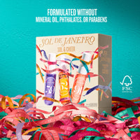 A boxed beauty product labeled SOL DE JANEIRO / SOL & CHEER stands upright on a bed of colorful ribbon strands against a bright turquoise background. The box shows three illustrated bottles in purple, orange, and peach tones with multicolored ribbon graphics.