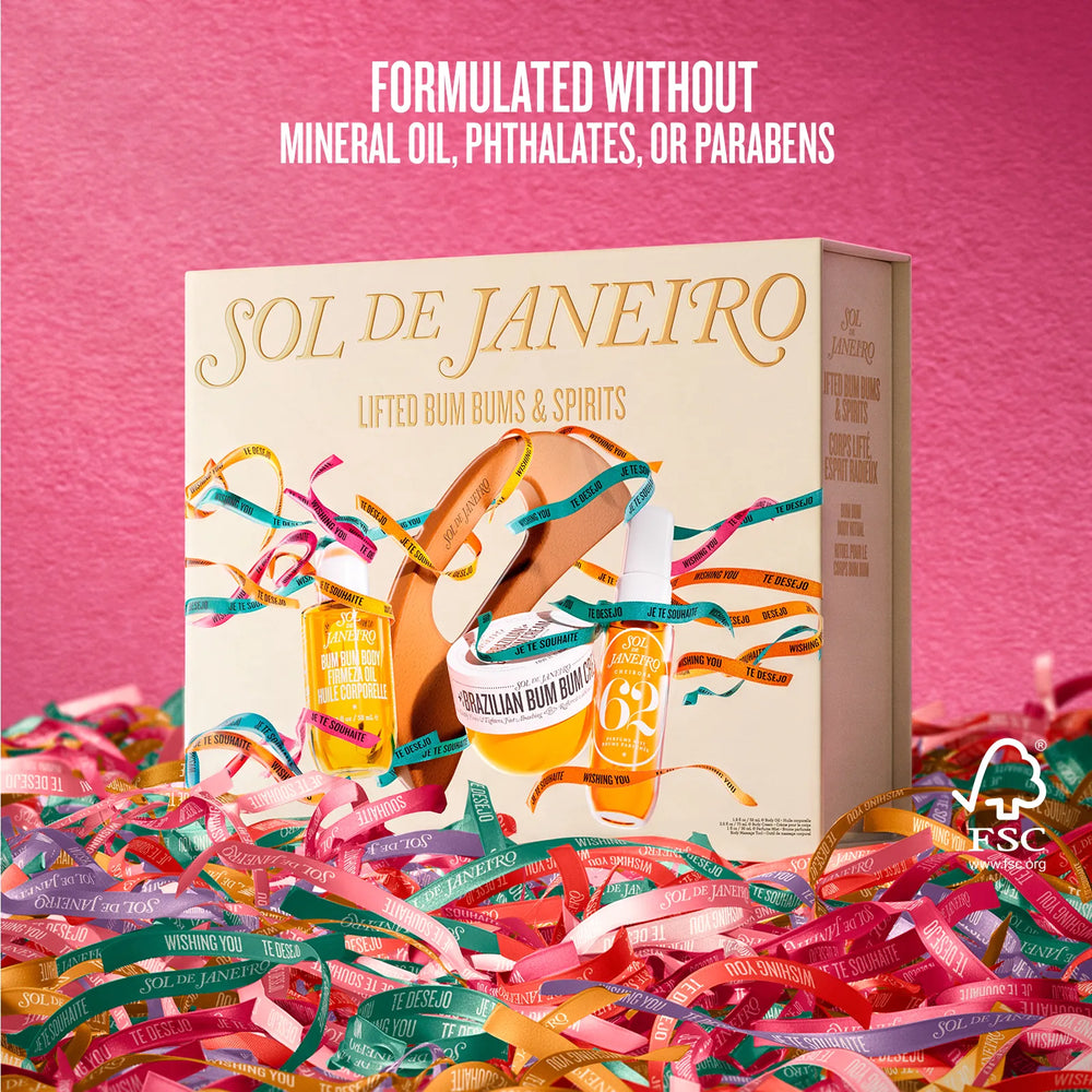 A boxed skincare gift set labeled SOL DE JANEIRO stands upright on a bed of colorful paper streamers against a pink background. The box shows illustrated bottles and jars with gold, teal, and peach accents.