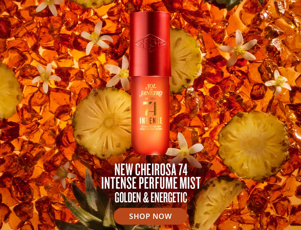 A red cylindrical perfume bottle labeled 'Cheirosa 74 Intense' stands upright on a glossy orange background made of glass fragments, pineapple slices, and small white flowers. White text at the bottom reads 'NEW CHEIROSA 74 INTENSE PERFUME MIST GOLDEN & ENERGETIC' with a 'SHOP NOW' button.