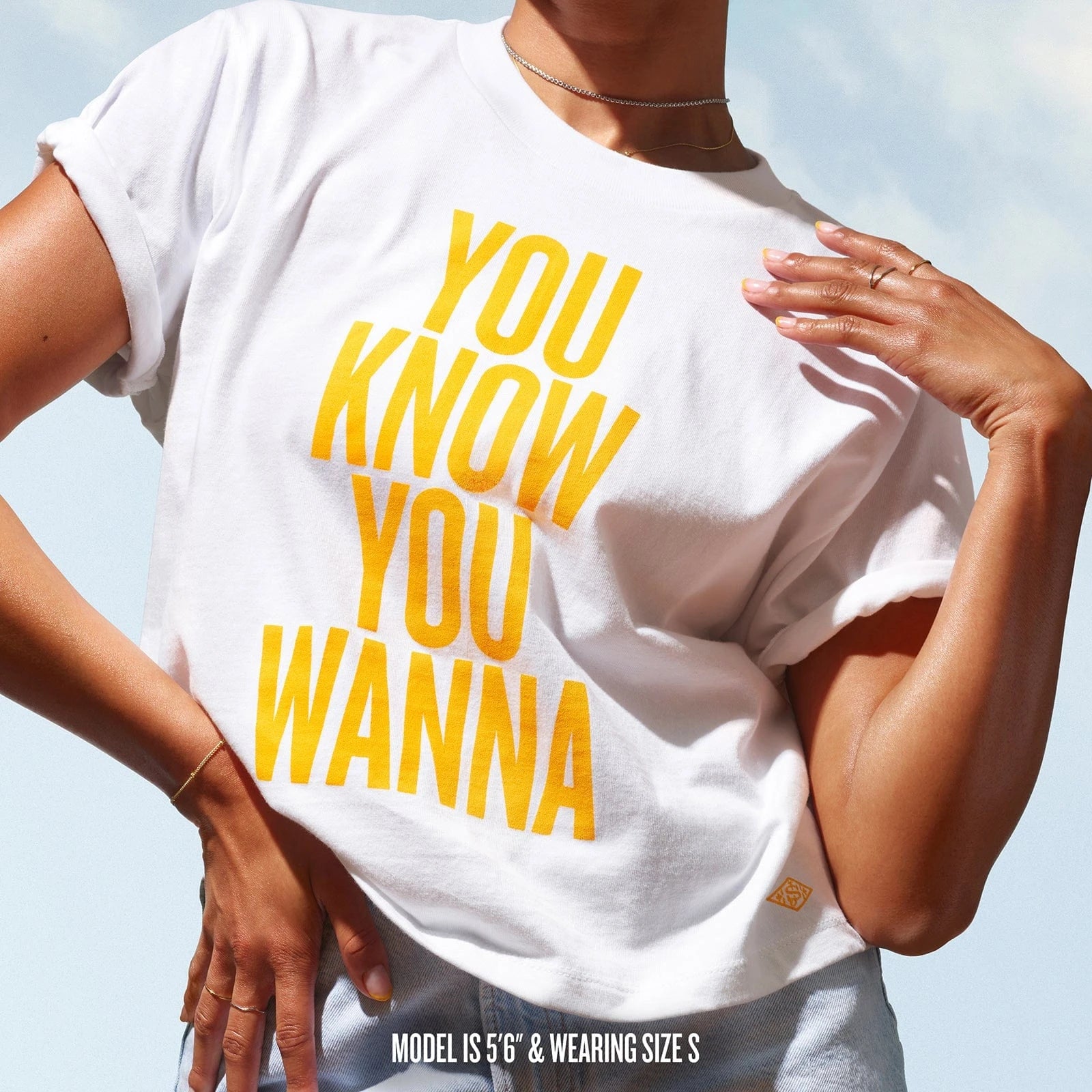 Front shot of the badalada t-shirt that reads "you know you wanna" in sol de janeiro yellow. T shirt is white