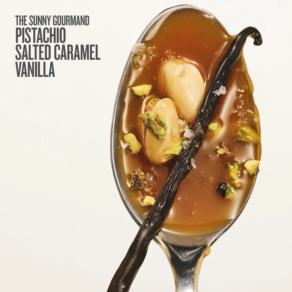 Spoon with dessert featuring salted caramel, vanilla beans, and pistachios on a white background.