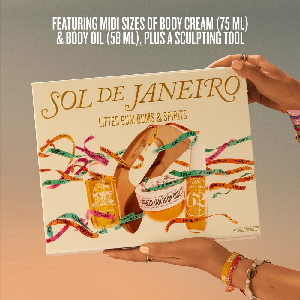 A person holds a boxed body care set labeled SOL DE JANEIRO against a soft beige-to-gray gradient background. The box features illustrated products including a body cream jar, body oil bottle, and a sculpting tool, with colorful ribbon graphics and the text 'FEATURING MIDI SIZES OF BODY CREAM (75 ML) & BODY OIL (58 ML), PLUS A SCULPTING TOOL.