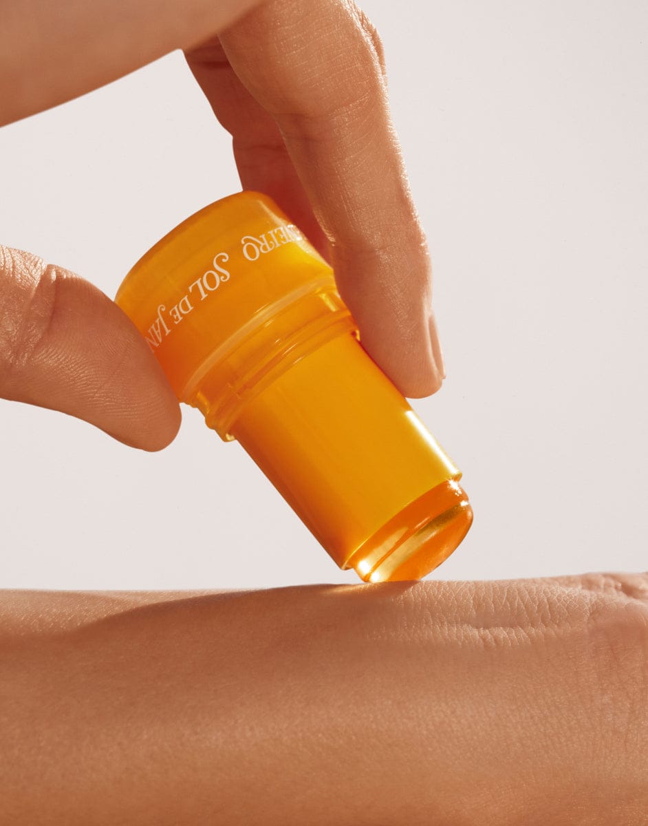 Person applying a yellow cosmetic product to their arm with a neutral background