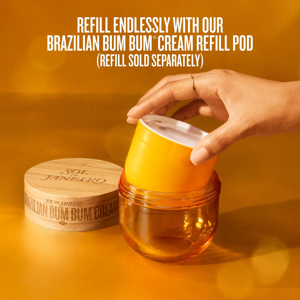 A hand inserts an orange-yellow cream refill pod into a clear amber jar, with a branded wooden lid beside it on a warm orange background. Text at the top reads: 'REFILL ENDLESSLY WITH OUR BRAZILIAN BUM BUM CREAM REFILL POD (REFILL SOLD SEPARATELY)'.