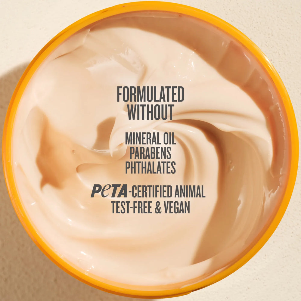Top-down view of a beige cosmetic cream in a round tub with a yellow-orange rim, featuring text that reads 'FORMULATED WITHOUT MINERAL OIL PARABENS PHTHALATES PETA-CERTIFIED ANIMAL TEST-FREE & VEGAN'.