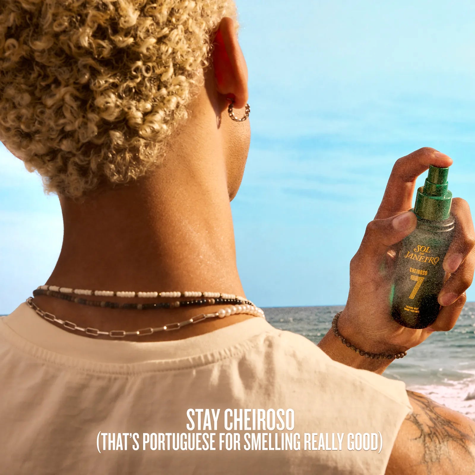 Person holding a spray bottle with a beach in the background, featuring the brand &