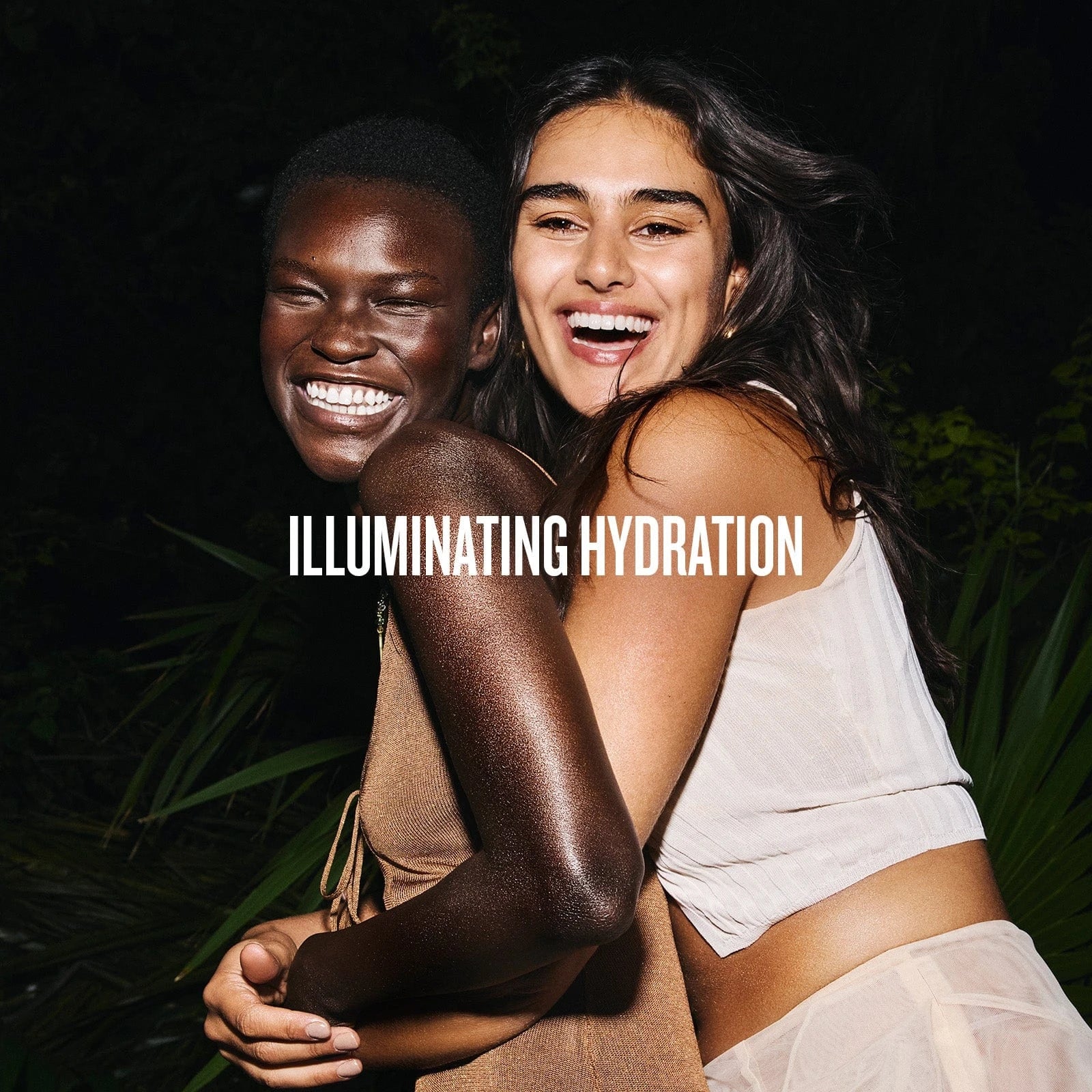 text on image reads illuminating hydration. This image is of two models miling and looking glowy wearing sol de janeiro glowmotions glow body oil