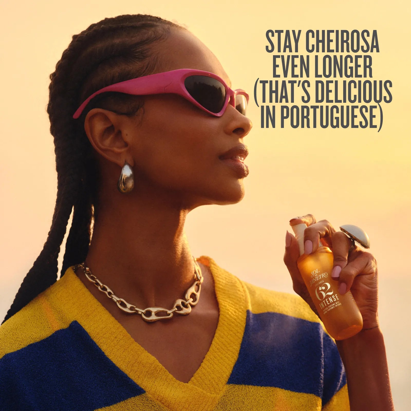 A woman in profile wearing pink sunglasses and a yellow-and-blue striped sweater holds a bottle of R2 Mafik perfume. The image has a warm sunset background and text that reads, &
