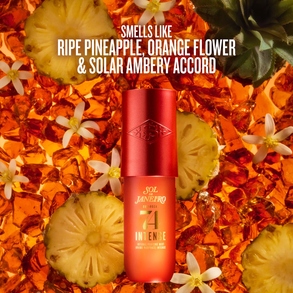 A red and orange cylindrical bottle of Sol Janeiro Intense sunscreen stands centered against a tropical background of sliced pineapple, white flowers, and amber liquid. White text at the top reads, 'SMELLS LIKE RIPE PINEAPPLE, ORANGE FLOWER & SOLAR AMBERY ACCORD.