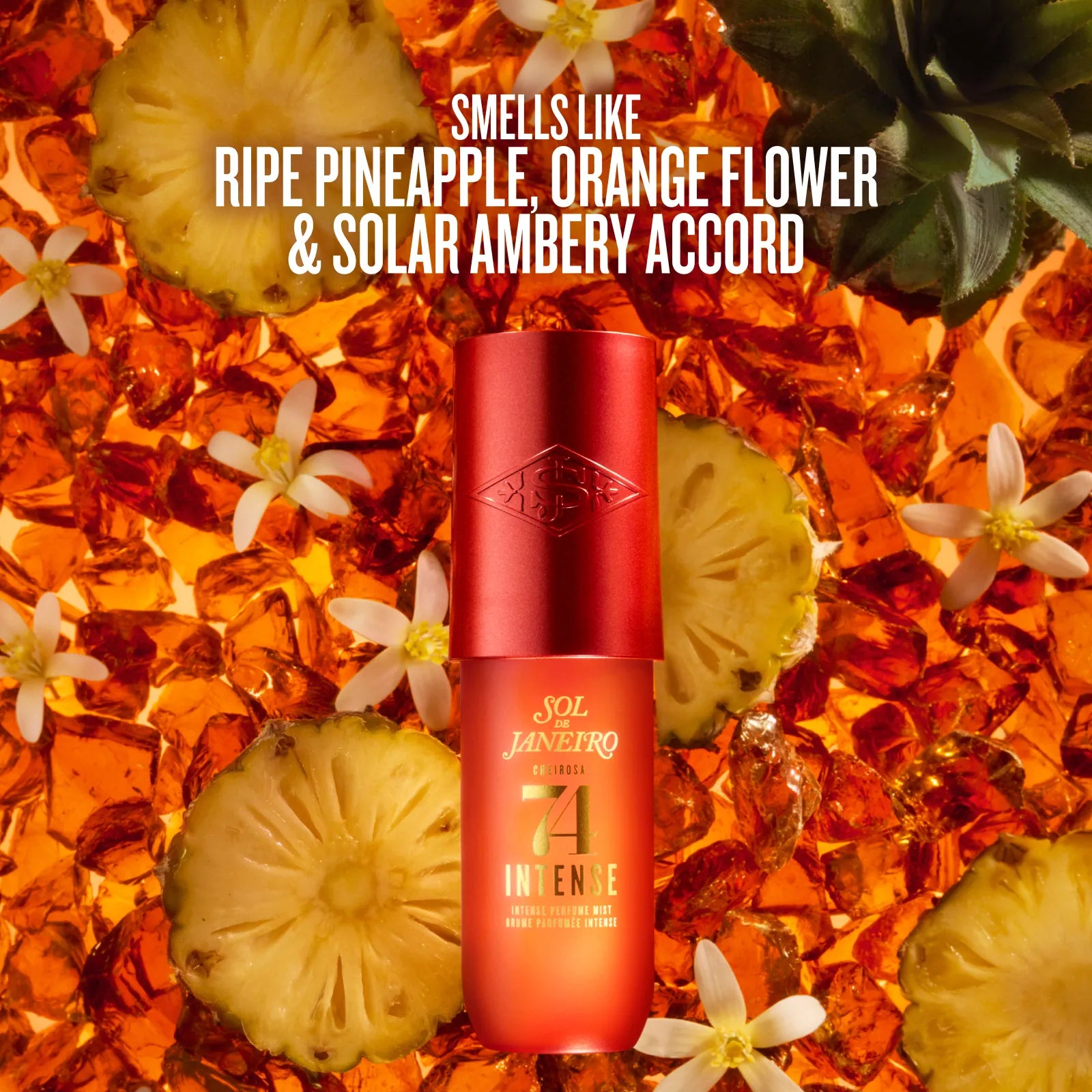 A red and orange cylindrical bottle of Sol Janeiro Intense sunscreen stands centered against a tropical background of sliced pineapple, white flowers, and amber liquid. White text at the top reads, 'SMELLS LIKE RIPE PINEAPPLE, ORANGE FLOWER & SOLAR AMBERY ACCORD.