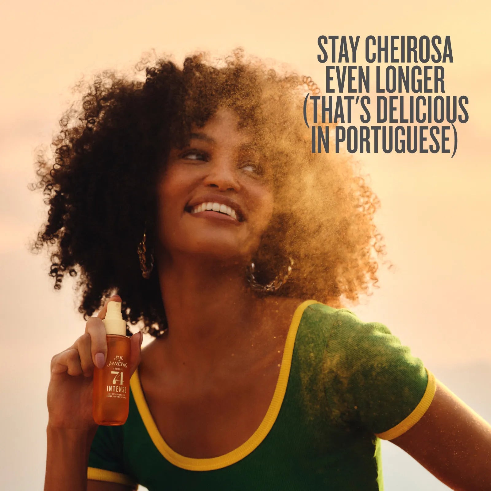 A smiling woman with voluminous curly hair holds a bottle of hair product in her hand, wearing a green and yellow top against a warm sunset sky. Text in the upper right reads, 'STAY CHEIROSA EVEN LONGER (THAT'S DELICIOUS IN PORTUGUESE)'.