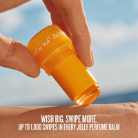 Person applying a yellow sunscreen stick on their arm with a blue sky background